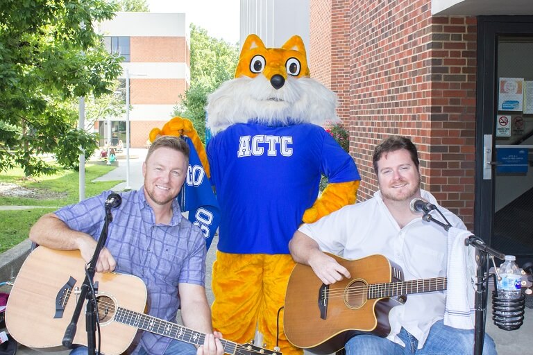 The pathfinder mascot with two musicians outside of the College Drive Campus